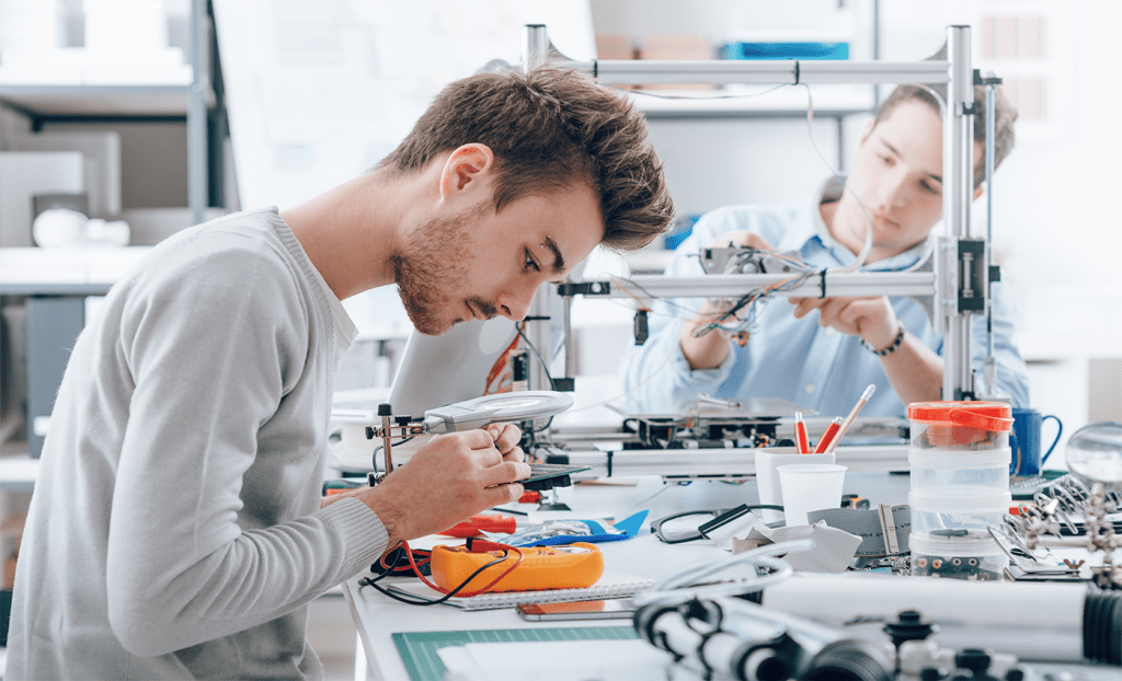 A production area showing 2 people assembling and testing electronic assemblies