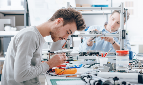 A production area showing 2 people assembling and testing electronic assemblies