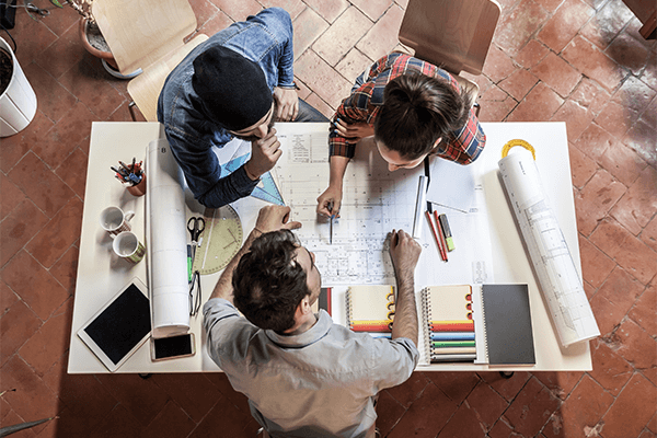 3 people around a desk discussing a design drawing