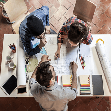 3 people around a desk discussing a design drawing